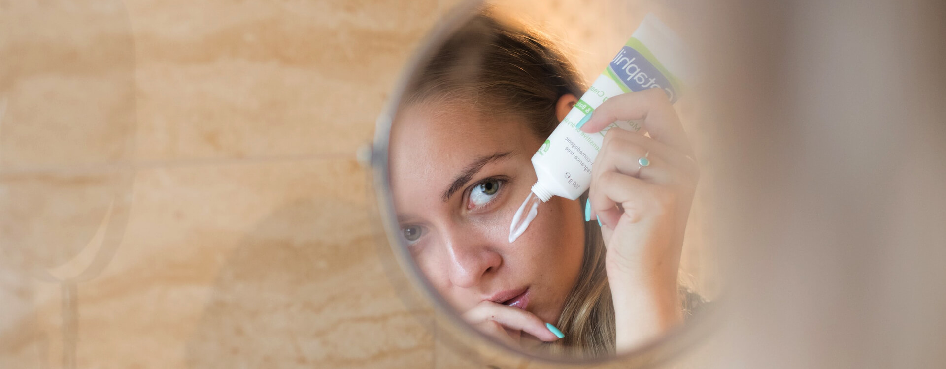 Žena v zrkadlovom odraze si natiera krém na tvár